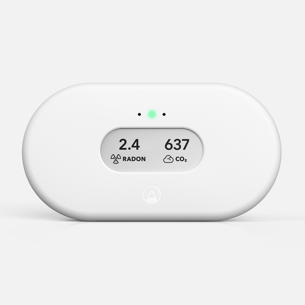 Airthings View Plus in white, seen from the front, its e-ink display reading radon 2.4 and CO2 637 with the Airthings logo button below and a green status light above, on a plain light-gray background