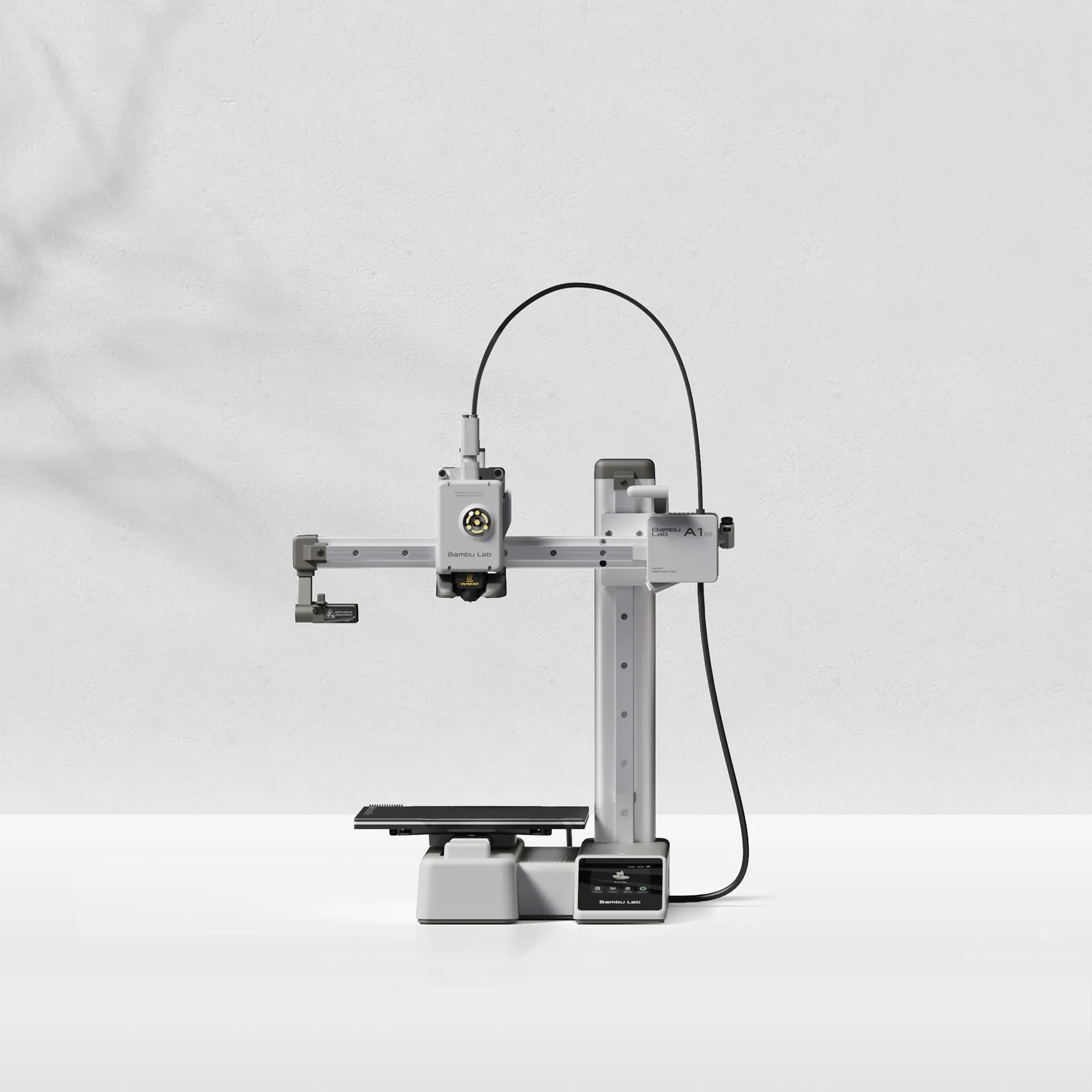 Bambu Lab A1 mini 3D printer in gray, its cantilever arm and toolhead above a small black build plate, the touchscreen on the base, against a light wall and tabletop