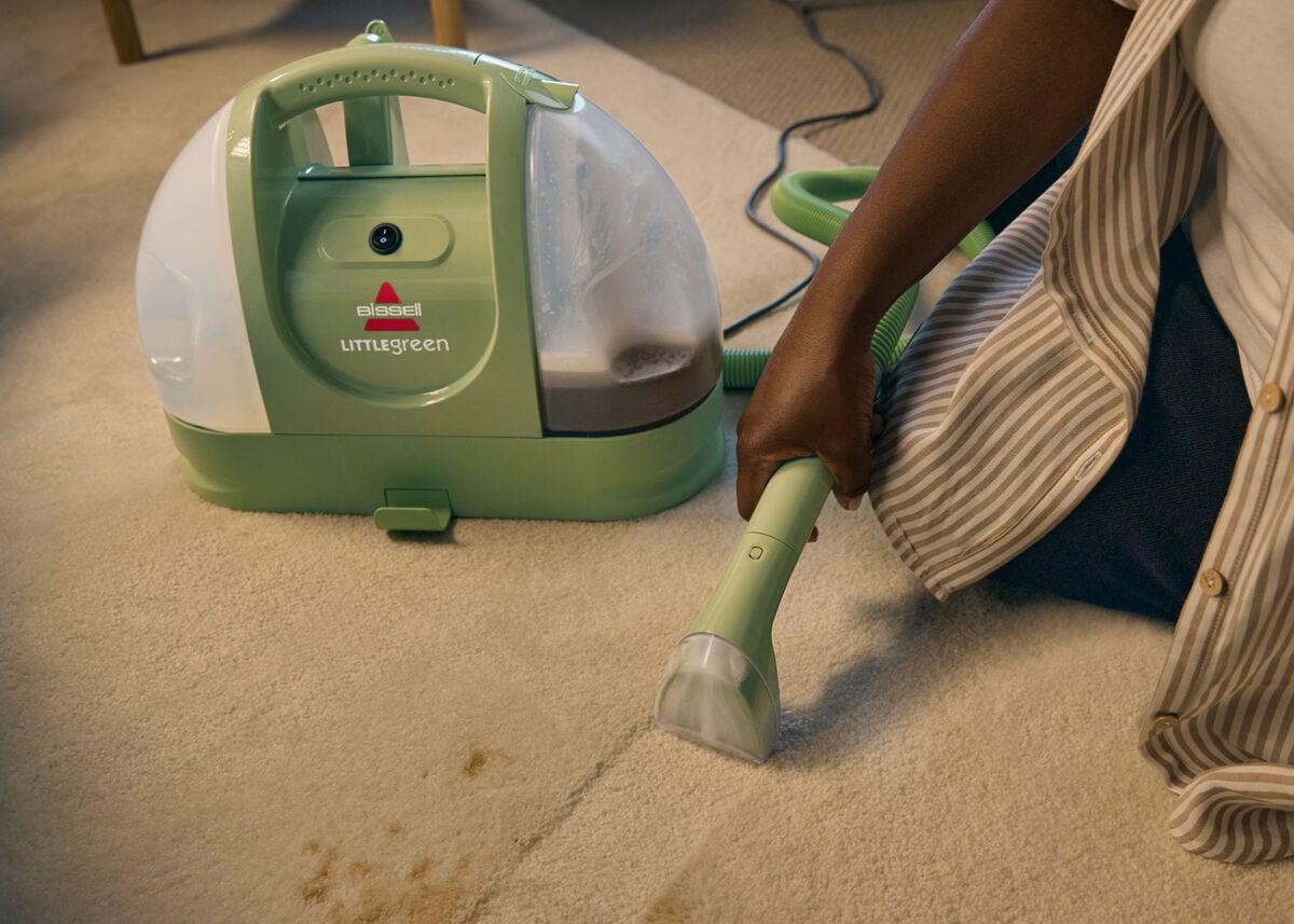 Green Bissell Little Green 1400B portable carpet cleaner on carpet with the hose and stain tool in use