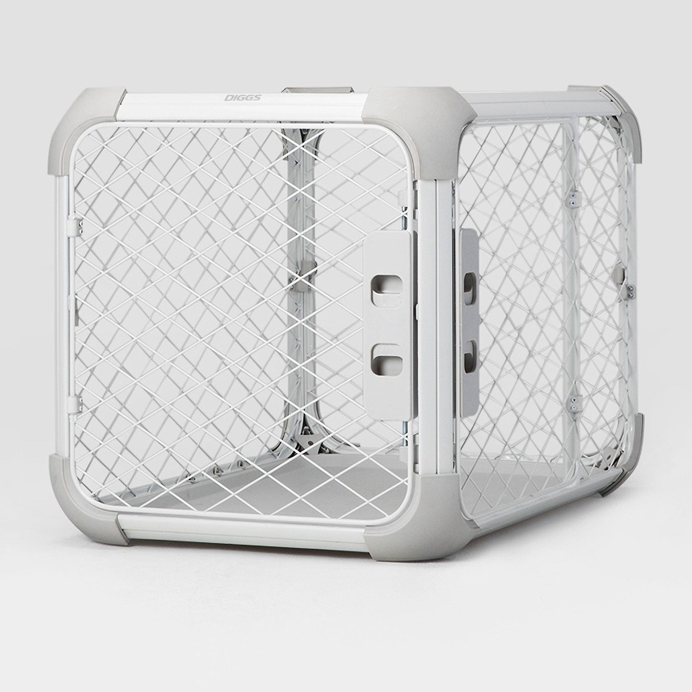 White-and-gray Diggs Evolv dog crate, closed, seen at an angle with the front panel facing the camera and one side panel receding to the right: diamond-mesh steel panels in rounded light gray plastic corners, small DIGGS lettering on the white top bar, two light gray slotted latch plates where the front panel meets the side, and a pale floor tray inside, on a light gray background