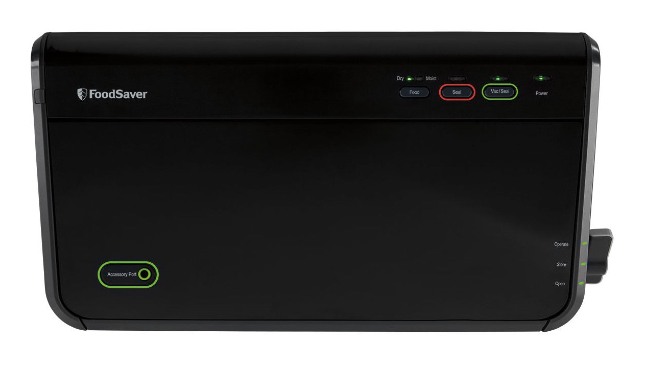 Black FoodSaver FM2100 vacuum sealer seen from directly above with the lid closed, showing the FoodSaver wordmark, the Dry/Moist, Food, Seal, Vac/Seal and Power controls, the green-ringed Accessory Port, and the latch marked Operate, Store and Open, on a white background