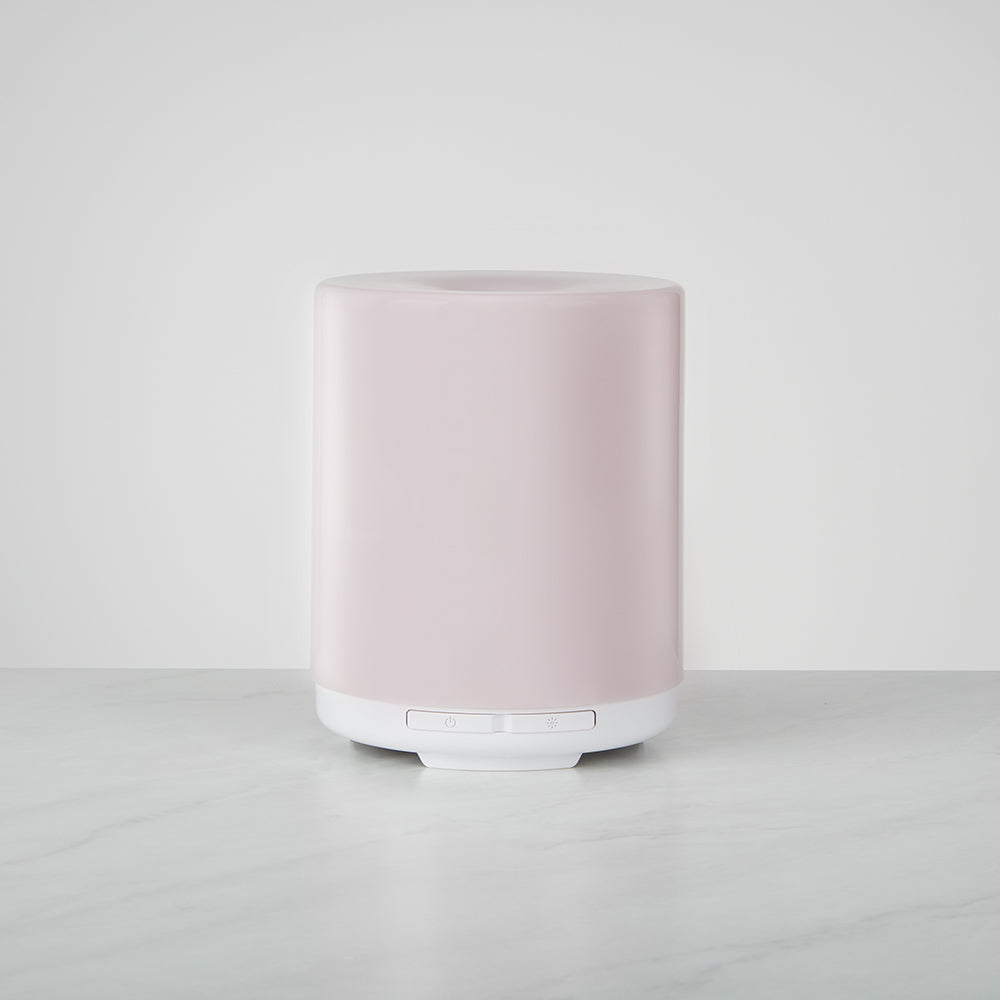 Ellia Voyage ultrasonic diffuser in soft pink with a white base and two buttons, standing on a marble surface against a plain light-grey wall