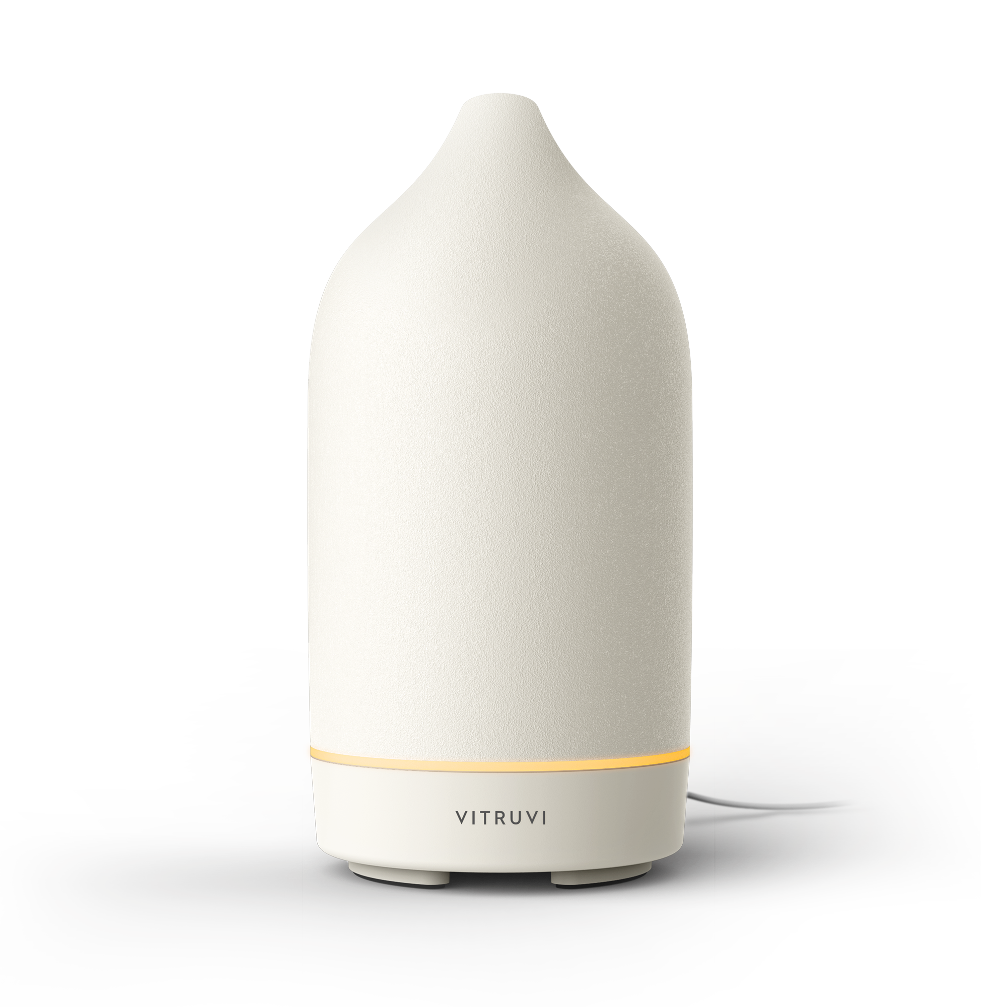Vitruvi Stone Diffuser in White standing upright, a warm amber light ring glowing at the seam above the VITRUVI wordmark on the base, with a white power cord trailing off to the right
