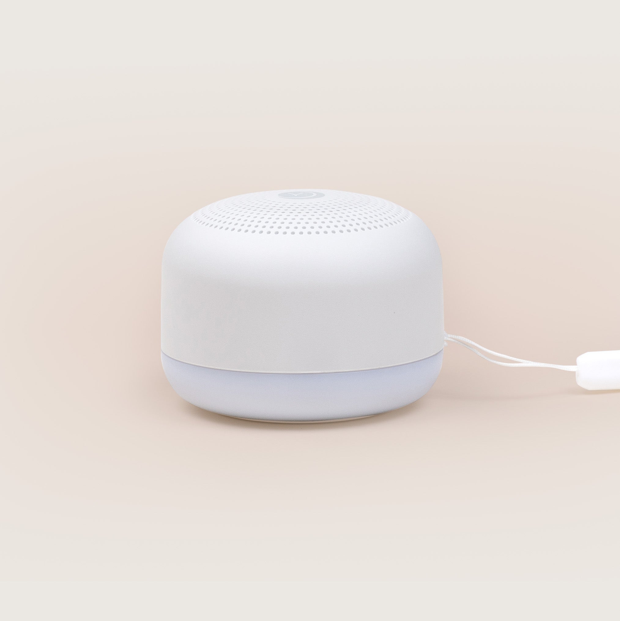 Yogasleep Travel Mini sound machine in white, a small round unit with a fabric-covered top and lanyard