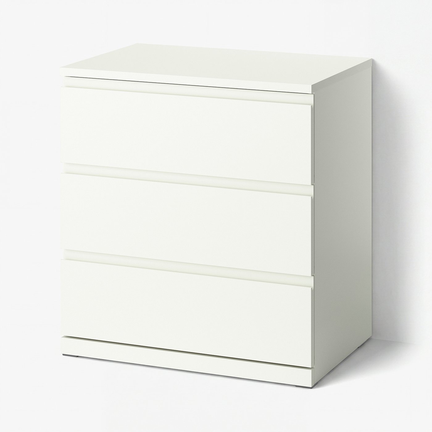 引き出し3段の白いIKEA STORKLINTAチェストを斜め前から写した製品写真。各引き出しの上縁に横一直線の取っ手の溝があり、下に台座が付いている、明るいグレーの背景